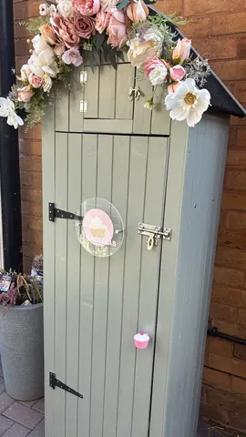 A small green shed with a pink sign on it.