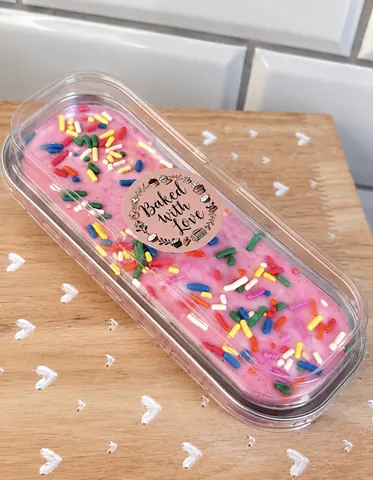 A container of pink cake with sprinkles on a wooden table.
