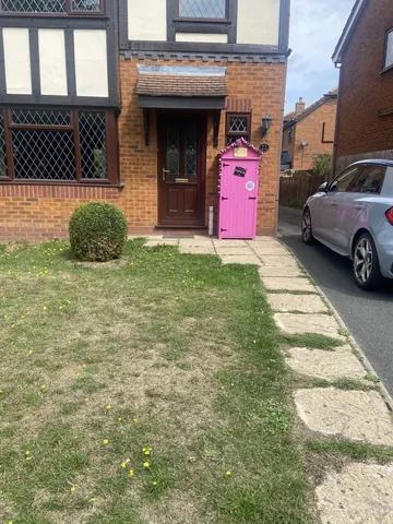 A pink door is sitting on a sidewalk next to a house.