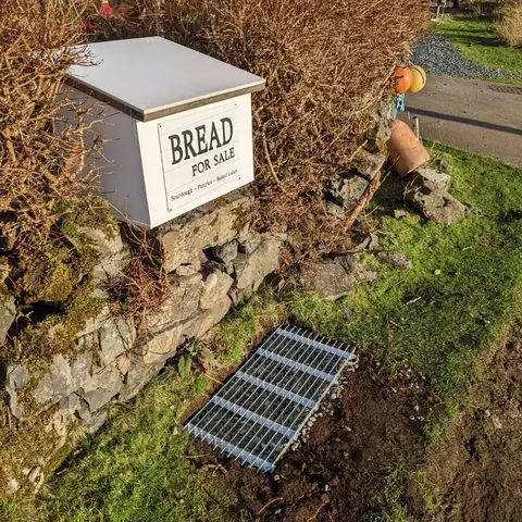 A sign for bread for sale is on a stone wall.