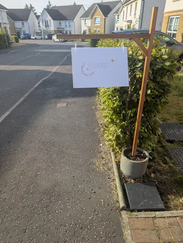 A sign is hanging on a wooden post in front of a bush.