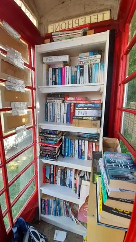 A red telephone booth with a bookshelf inside.