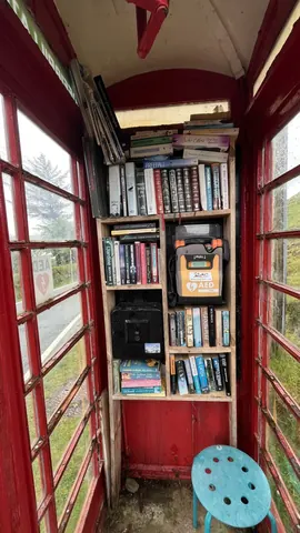 A red telephone booth with a bookshelf inside.