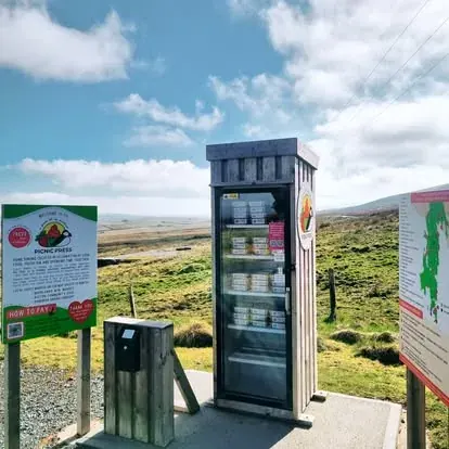 A small refrigerator is sitting on a concrete slab in a field.