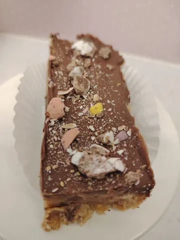 A piece of chocolate cake with white frosting and sprinkles on a white plate.