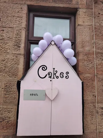 A pink house with a sign that says "Cakes" and balloons.