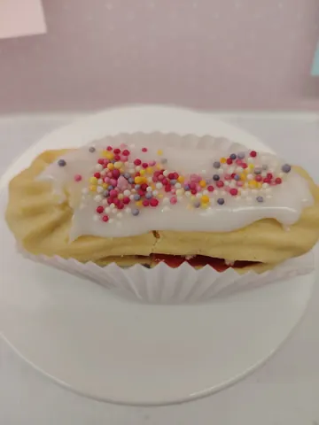 A pastry with white frosting and sprinkles on a white plate.