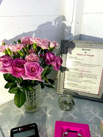A vase of pink flowers sits on a table next to a sign.