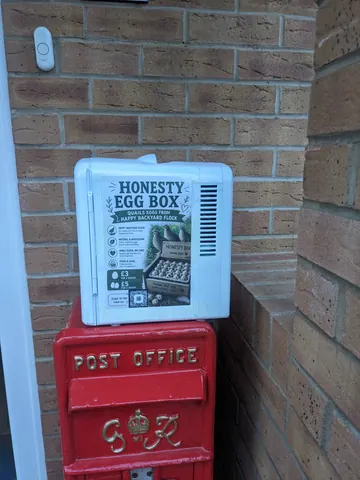 A red mailbox with a white box on top of it.