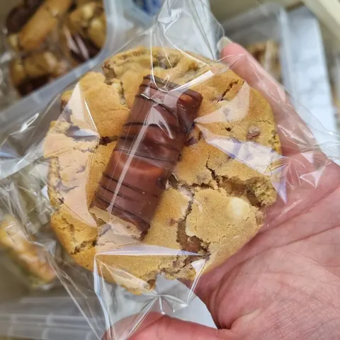 A person is holding a cookie with chocolate and caramel toppings.