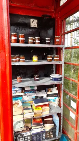 A red telephone booth with a shelf full of books.