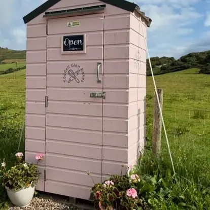 A pink outhouse with a sign that says open.