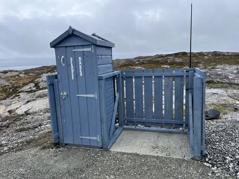 A blue outhouse with a white door.