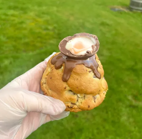 A person is holding a cookie with chocolate and cream on it.