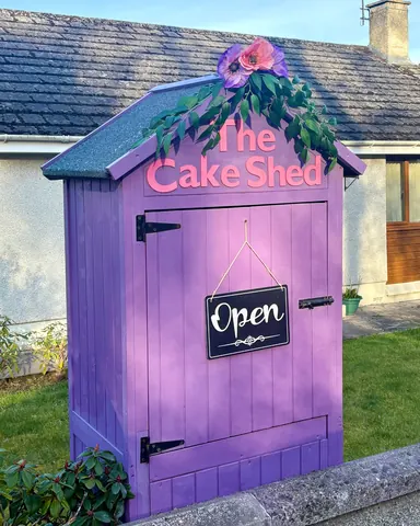 A purple shed with a sign that says "The Cake Shed" on it.