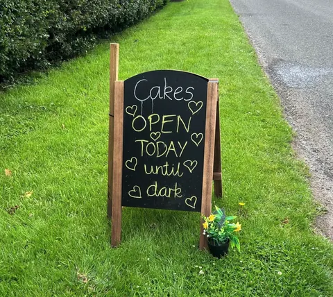 A sign advertising cakes is displayed on a wooden post.