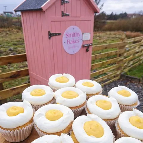 A pink building with a sign that says "Smitty Bakes" and a stack of cupcakes.