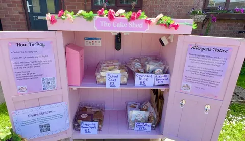A pink and white cake stand with a sign that says "The Cake Shed".
