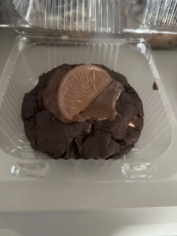 A chocolate cookie with chocolate frosting and a slice of orange on top.