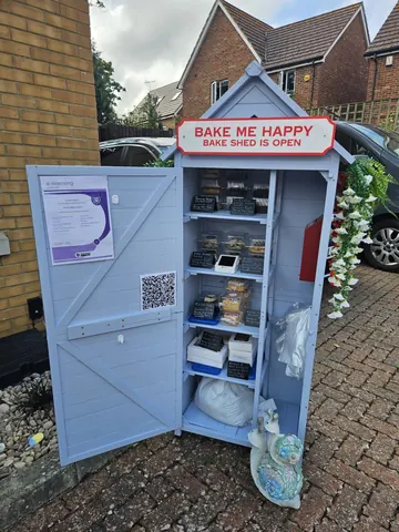 A blue shed with a sign that says "Bake me happy" on it.