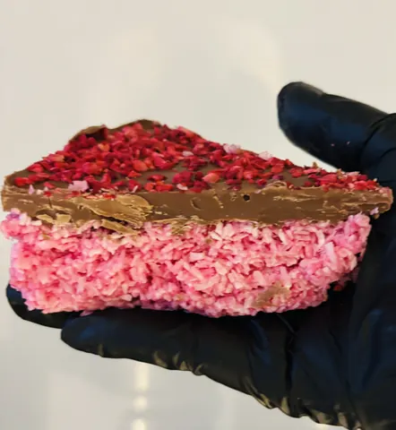 A hand holding a piece of chocolate cake with pink frosting.