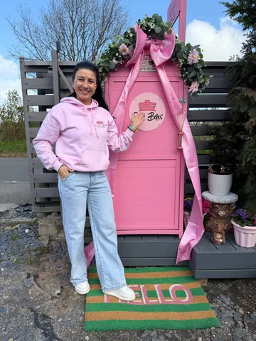 A woman in a pink hoodie standing in front of a pink door.