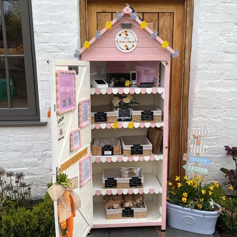 A small pink house with a clock on the door.