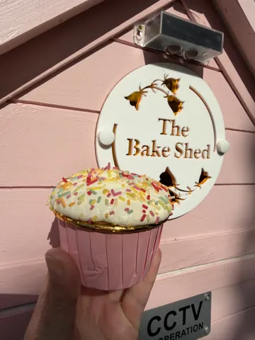 A person is holding a cupcake in front of a sign.