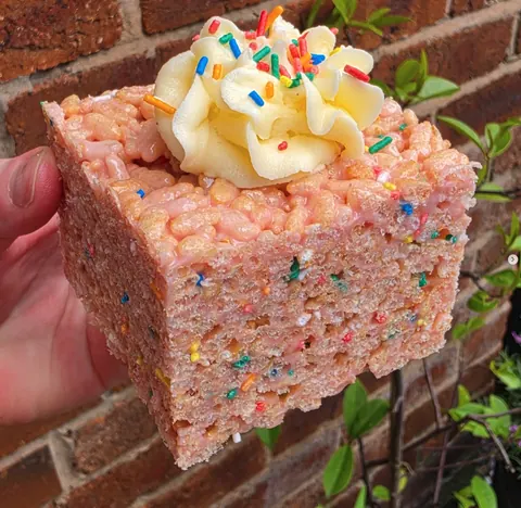 A hand holding a cake with sprinkles on top.