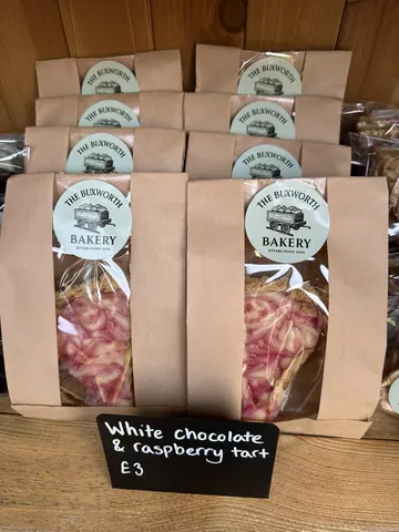 A sign that says "white chocolate & raspberry tart" is on a table.