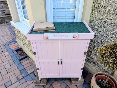 A pink and white cake stand with a sign that says "The Cake Away" on it.