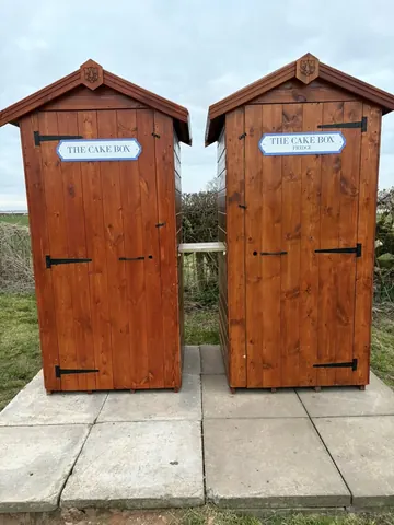 Two wooden outhouses with the words "The Cake Box" written on them.