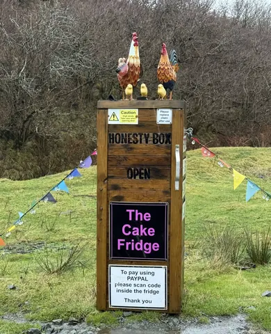 A sign for a cake fridge is on a wooden post.