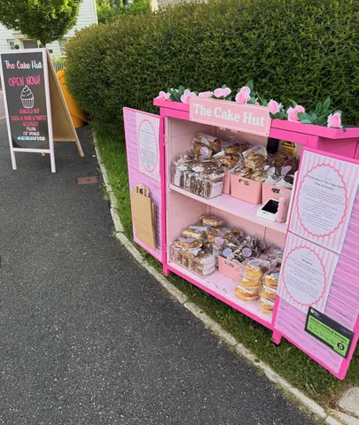 A pink and white cake stand with a sign that says "The Cake Hut" on it.