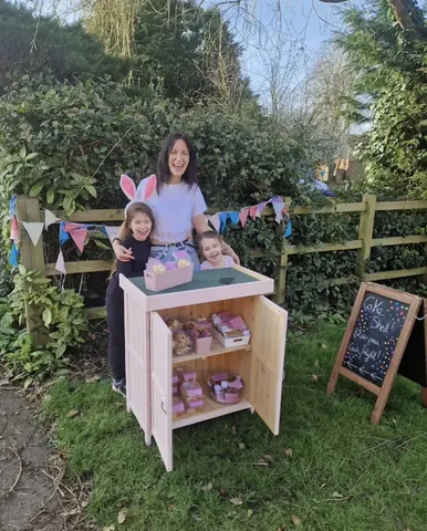 A woman and two children are standing in front of a pink box.