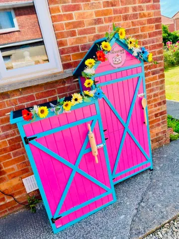 A pink and blue shed with flowers on it.