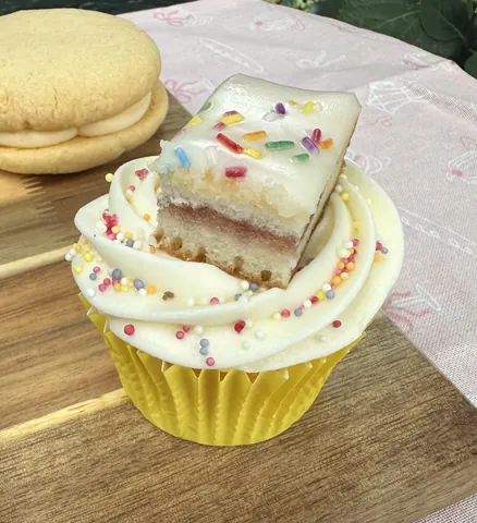 A cupcake with white frosting and sprinkles on a table.
