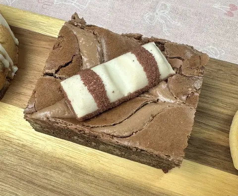 A piece of chocolate cake with white icing on a wooden cutting board.