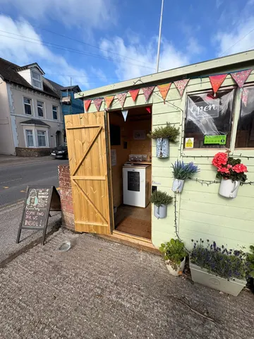 A small green building with a white sign on the side of the road.