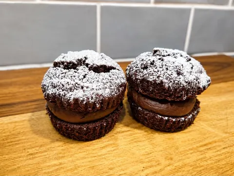 Two chocolate cupcakes with white powdered sugar on top.