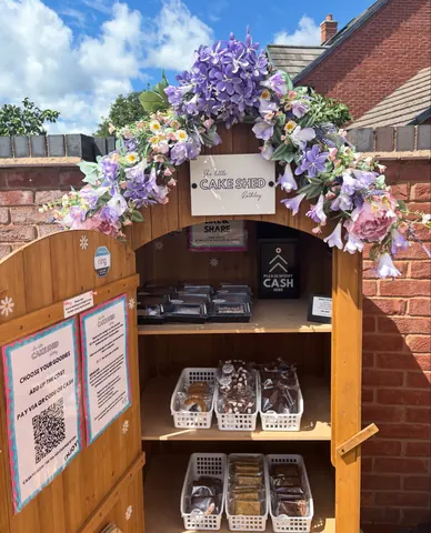 A wooden structure with a sign that says "Cake Shed" and a white sign that says "Welcome to the Cake Shed".