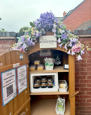 A wooden structure with a sign that says "Cake Shed" and a purple flower display.