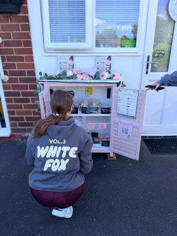 A woman is kneeling in front of a pink vending machine.