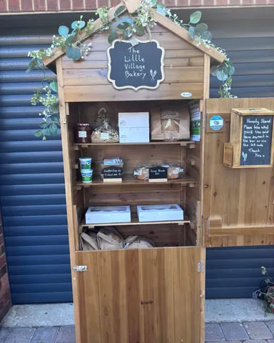 A wooden structure with a sign that says "The Little Village Bakery" on it.