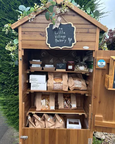 A wooden structure with a sign that says "The Little Village Bakery".