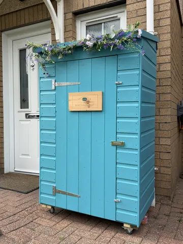 A blue shed with a wooden door and a sign on it.