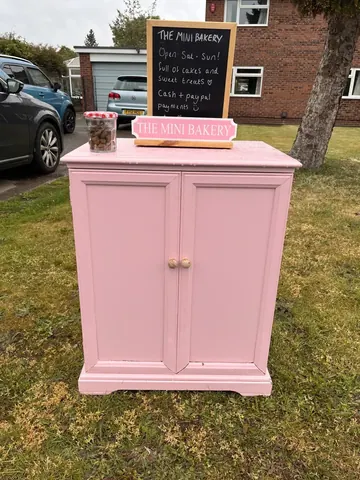 A pink cabinet with a sign on it that says "The Mini Bakery".