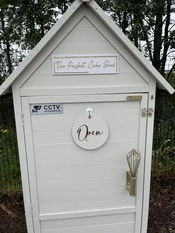 A white shed with a door and a sign that says "The Patio Cafe".