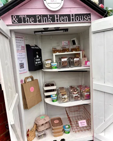 A small white building with a pink roof and a sign that says "& the pink hen house".