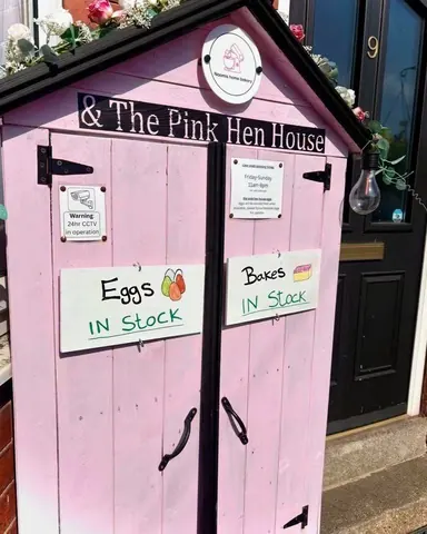 A pink shed with a sign that says eggs in stock.